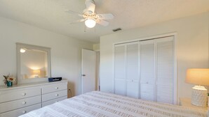 Une chambre à coucher comprenant un lit, une commode, un miroir, un ventilateur de plafond et un placard.