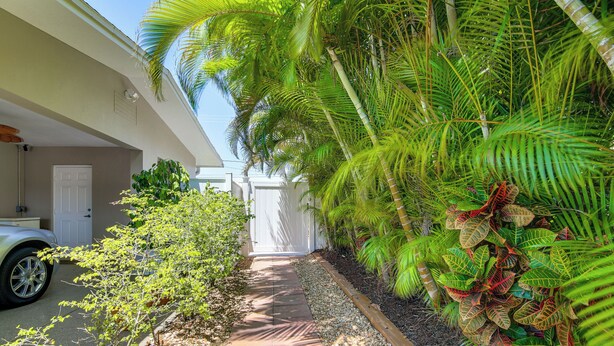 A pathway leading to a white garage door, surrounded by lush greenery and a white fence. - 1 Mi to Vanderbilt Beach! Walkable Couples Haven (Naples)