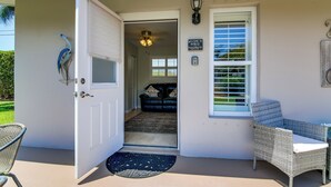 A house entrance with a door, a welcome mat, a wicker chair, a ceiling fan, and a view into the living room. - 1 Mi to Vanderbilt Beach! Walkable Couples Haven (Naples)