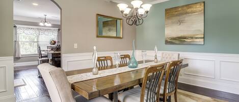 A dining room with a wooden table, upholstered chairs, a chandelier, and a painting on the wall.