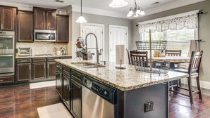 A kitchen with dark wood cabinets, stainless steel appliances, a granite countertop island, and pendant lighting. - Spacious Group Hub! Walk to Tribble Mill Park (Lawrenceville)