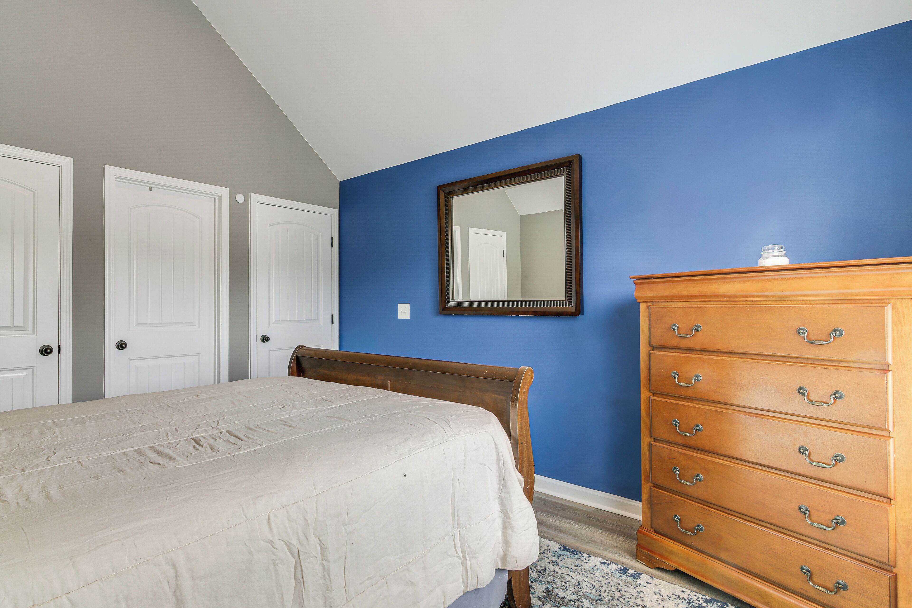 Een slaapkamer met een bed, een dressoir en een spiegel aan een blauwe muur.