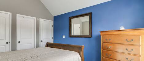 Een slaapkamer met een bed, een dressoir en een spiegel aan een blauwe muur.