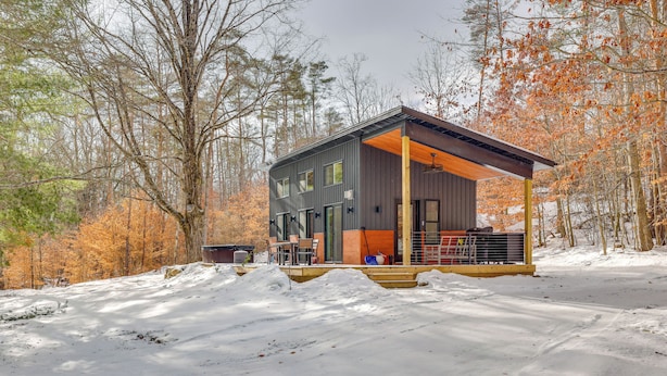 A modern cabin with a covered porch, surrounded by a snowy landscape and autumn-colored trees. - Hike, Fish & Unwind: 2-cabin Retreat in Hersey (Hersey)