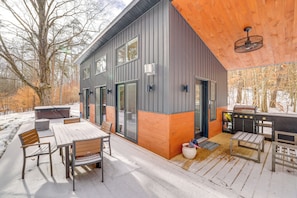 A modern outdoor deck with a wooden table and chairs, a barbecue grill, and a hot tub. - Hike, Fish & Unwind: 2-cabin Retreat in Hersey (Hersey)