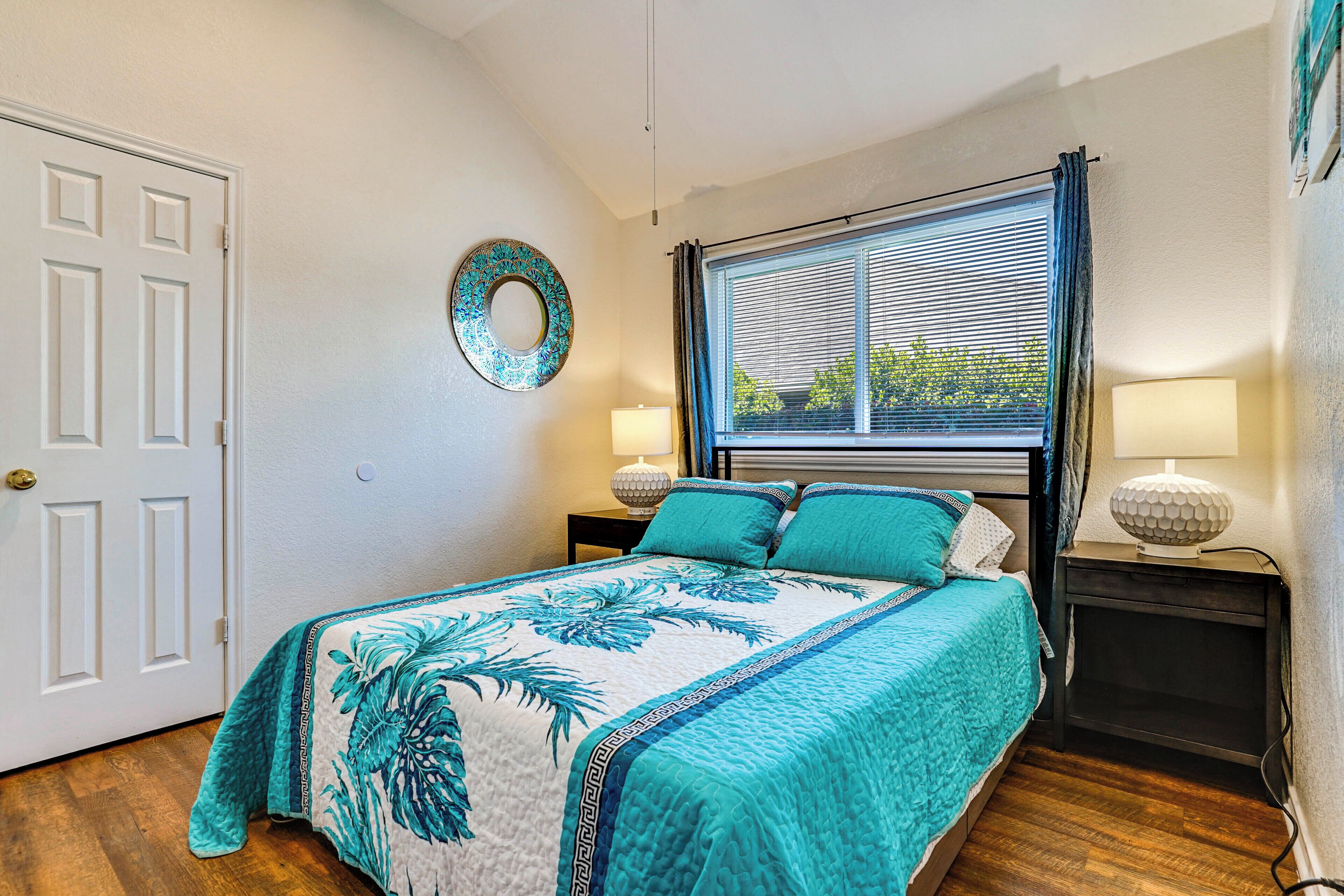 A bedroom with a bed, a window with blinds, a door, and a wall-mounted lamp.