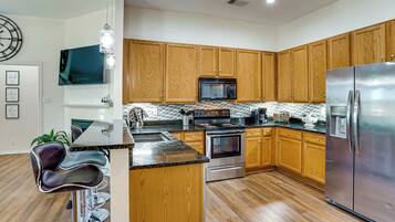 A modern kitchen with wooden cabinets, stainless steel appliances, and a bar area with stools.