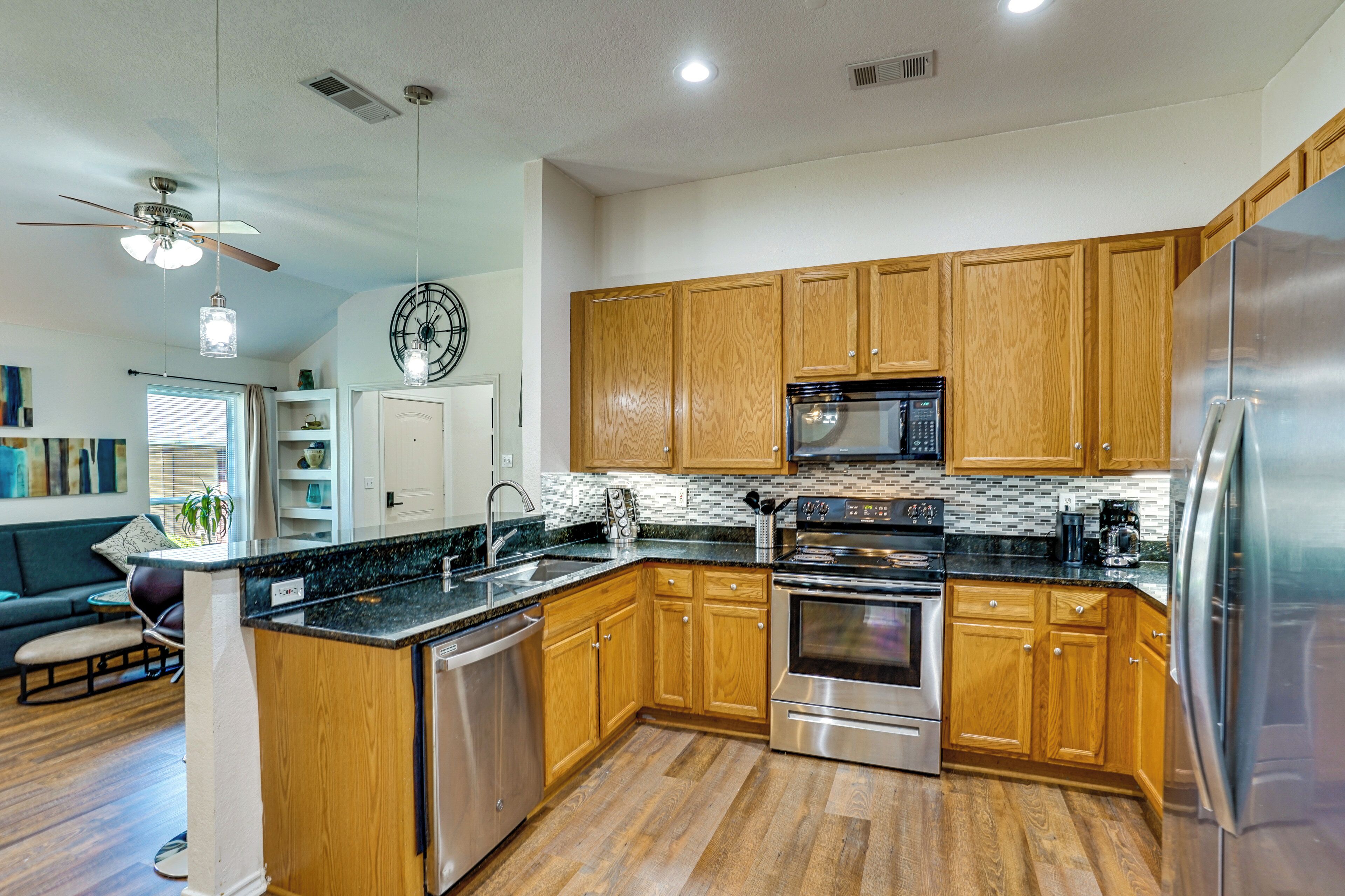 A modern kitchen with wooden cabinets, stainless steel appliances, a black countertop, and a ceiling fan.