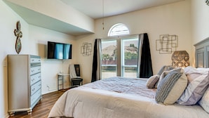 Een slaapkamer met een bed, een dressoir, een televisie en een raam met gordijnen.