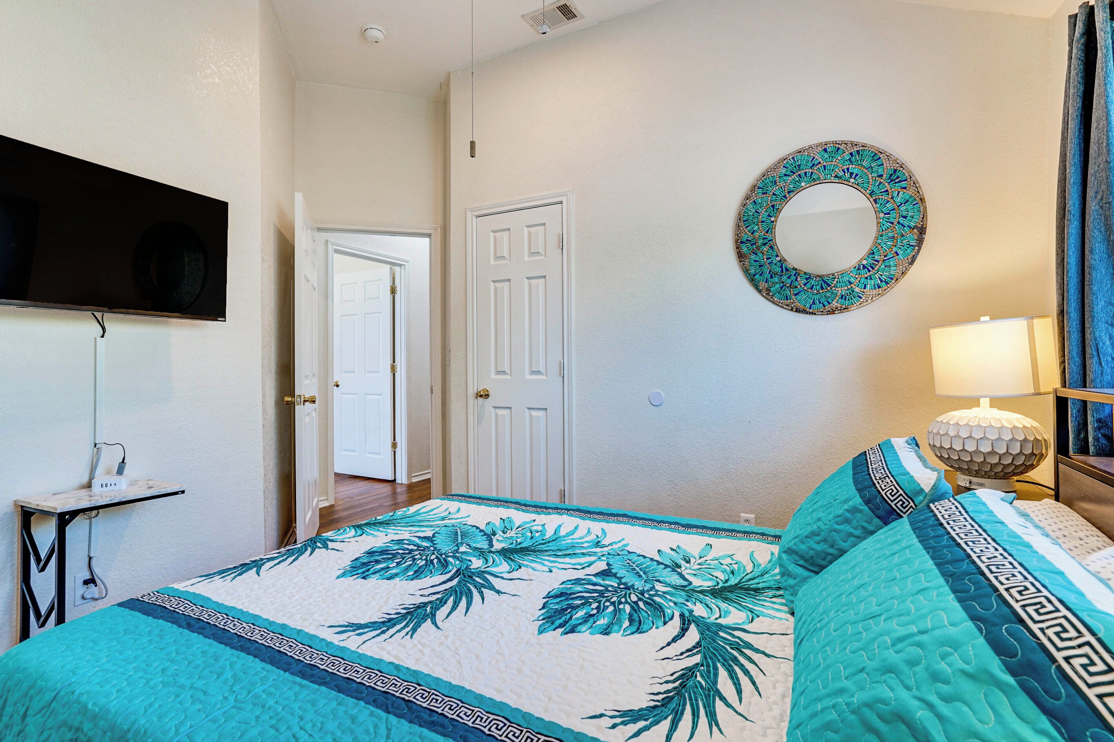 A bedroom with a bed, a television mounted on the wall, a door, and a mirror.