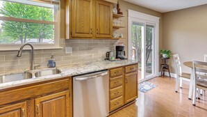 A kitchen with wooden cabinets, a dishwasher, a sink, and a dining area with chairs. - 13 Mi to Kauffman Stadium! 'cottontail Cottage' (Blue Springs)