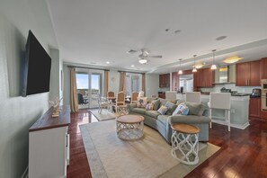 Ein modernes Wohnzimmer mit einer Couch, einem Couchtisch und einem Essbereich. Es gibt eine Küche mit Holzschränken und einem Kühlschrank.