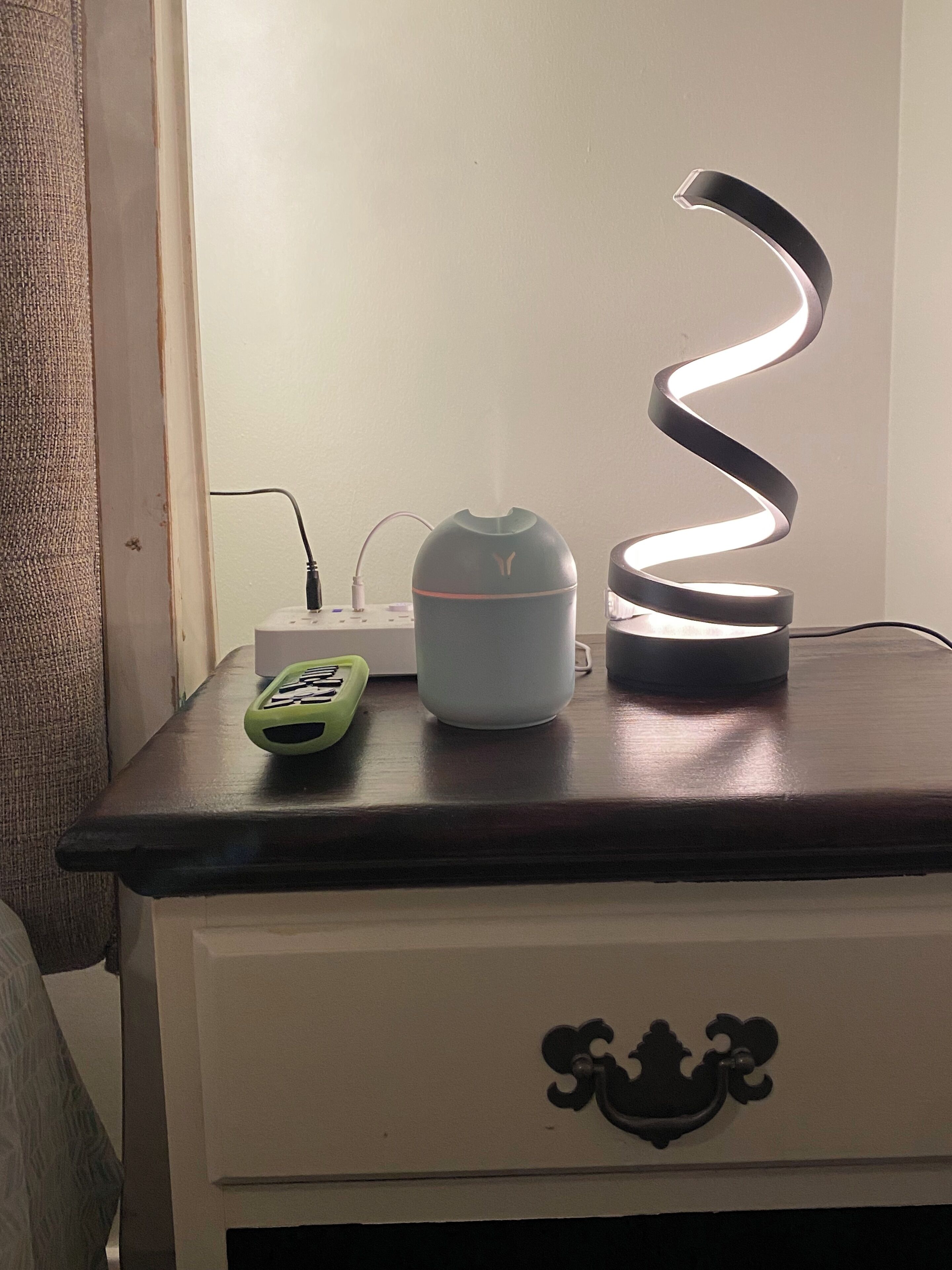 A bedside table with a lamp, a remote control, and a power strip.
