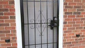 A black metal gate with a keypad lock, set in a brick wall with a white trim.