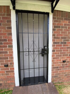 A black metal gate with a keypad lock, set in a brick wall with a white trim. - Cozy 1-bedroom studio in enjoyable Jackson with AC (Jackson)
