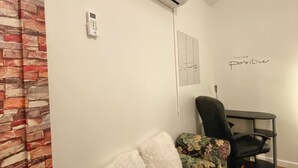 A room with a sofa, an air conditioning unit, a desk, and a motivational quote on the wall.