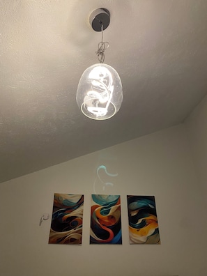 A ceiling light fixture with a clear glass cover, three abstract paintings on a white wall, and a white switch. - Cozy 1-bedroom studio in enjoyable Jackson with AC (Jackson)