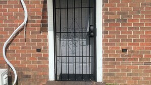 A brick building with a metal gate, a small overhang above the door, and a hose connected to a wall socket.