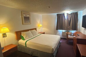 A hotel room with a bed, two bedside lamps, a desk, a chair, and a television. - Tacoma Port Inn Fife I-5 (Fife)