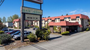 A hotel with a red roof, a bar and grill sign, and a parking lot with several cars.