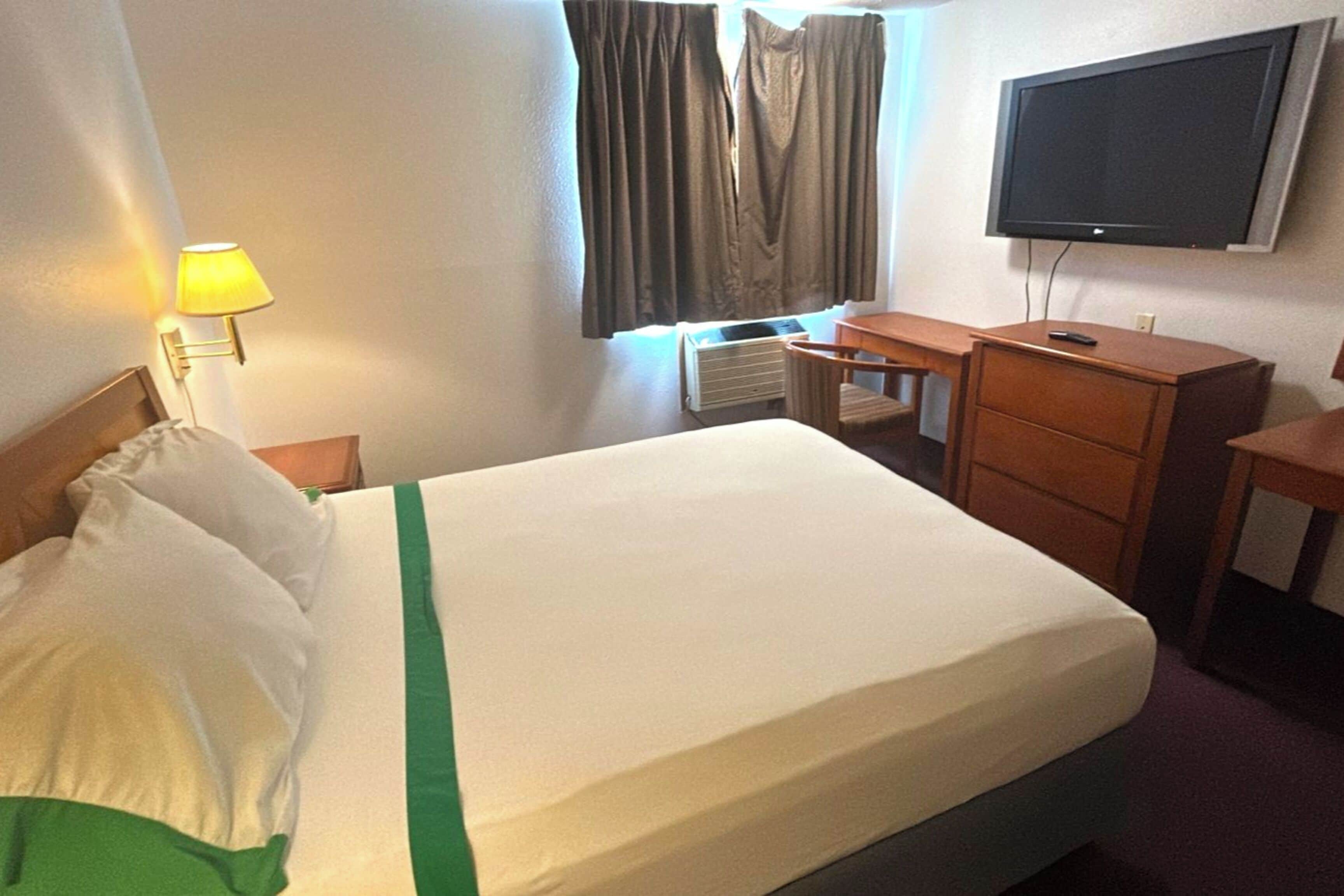 A hotel room with a bed, a desk, a chair, a TV, and a lamp.