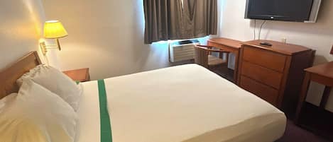 A hotel room with a bed, a desk, a chair, a TV, and a lamp.