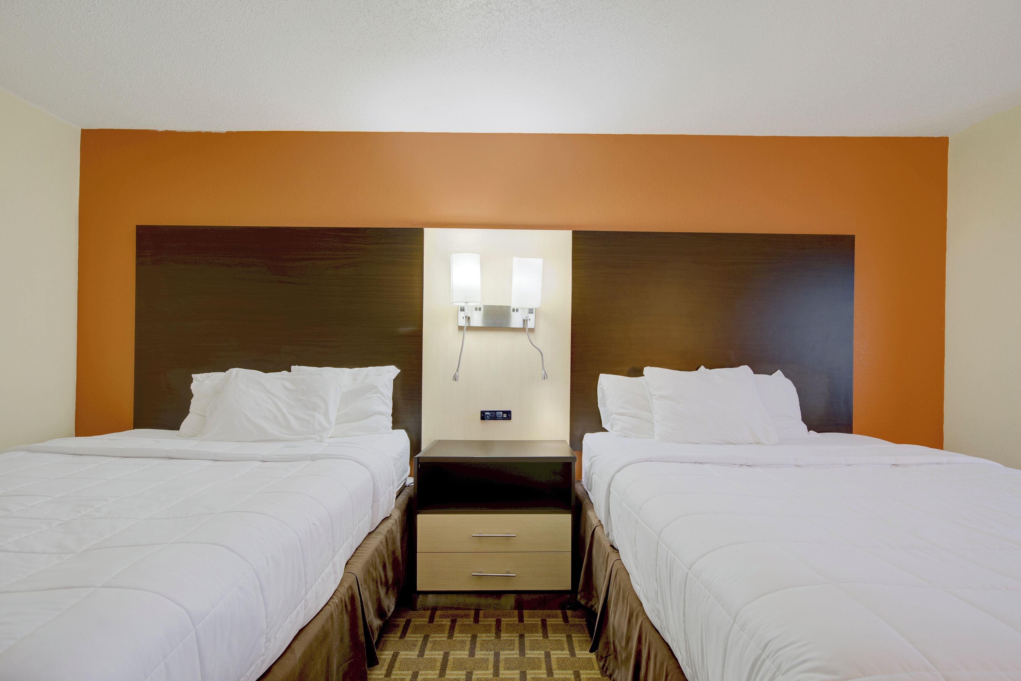 Een hotelkamer met twee bedden, een nachtkastje en een wandlamp.