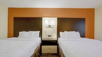 Una habitación de hotel con dos camas, una mesita de noche y una lámpara fijada a la pared.
