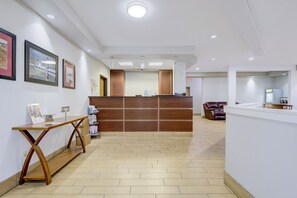 A reception area with a wooden reception desk, a small table with a sign, and framed pictures on the wall. - Saint Joseph Inn & Suites Benton Harbor Near I-94 (Benton Harbor)