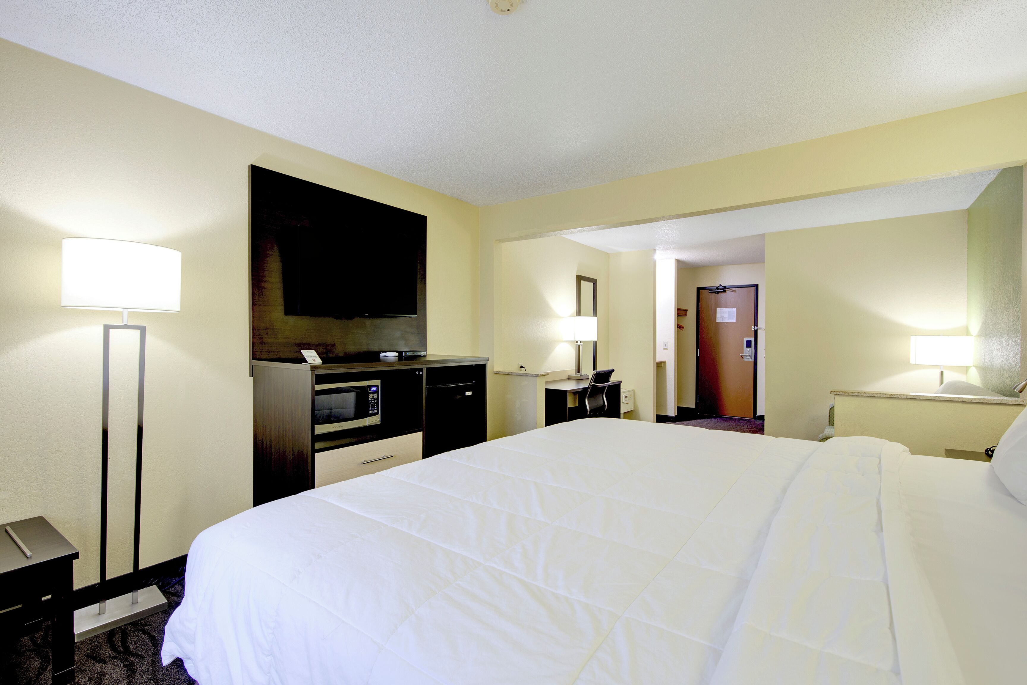 Ein Hotelzimmer mit einem großen Bett, einem Schreibtisch mit Computer, einem Flachbildfernseher und einer Mikrowelle.