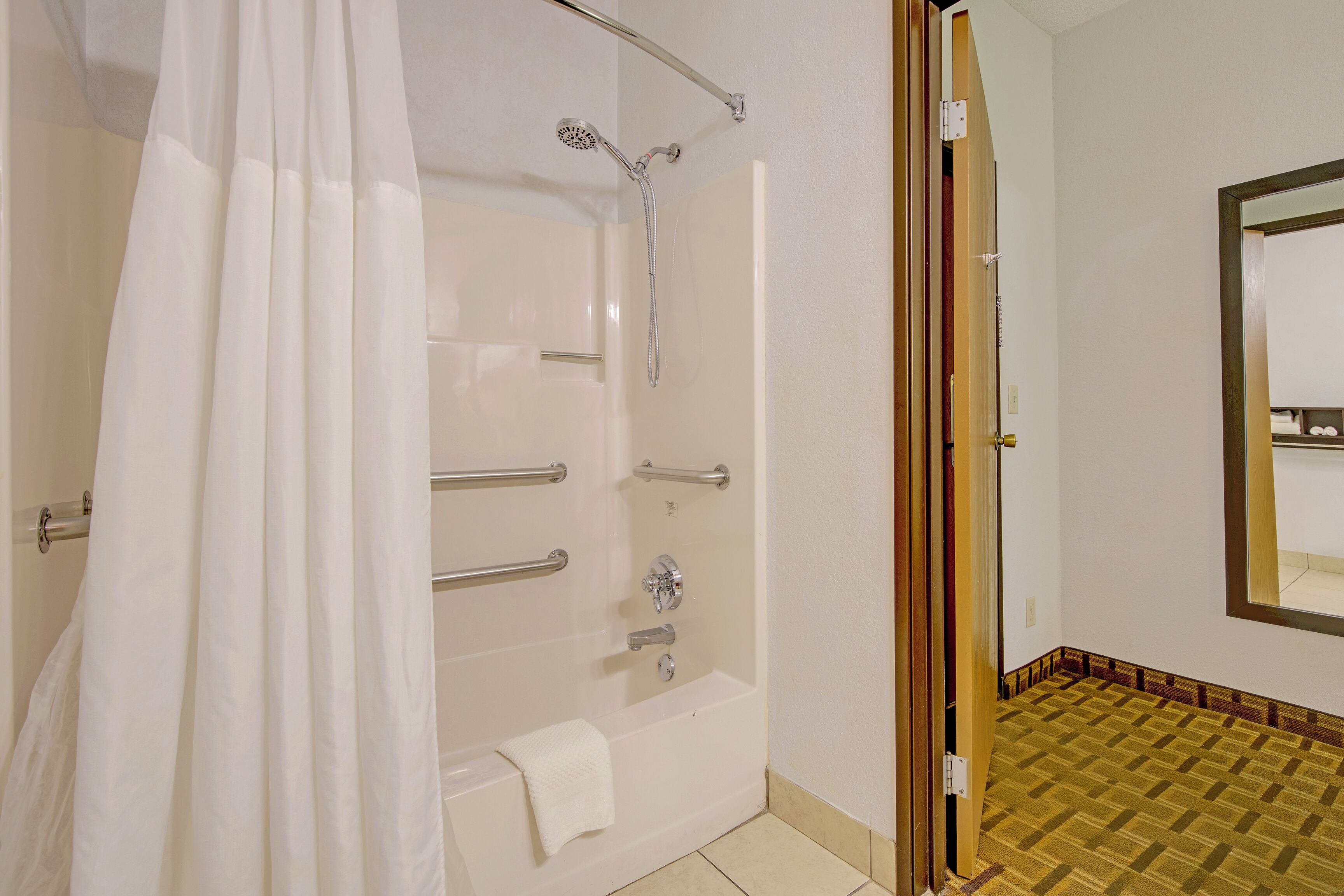 A bathroom with a shower, a bathtub, and a toilet. There are grab bars installed for safety.