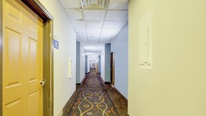A hotel hallway with carpeted floors, doors on both sides, and a sign indicating restrooms. - Saint Joseph Inn & Suites Benton Harbor Near I-94 (Benton Harbor)