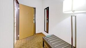 A hotel hallway with a wooden door, a mirror, a floor lamp, and a bench. - Saint Joseph Inn & Suites Benton Harbor Near I-94 (Benton Harbor)