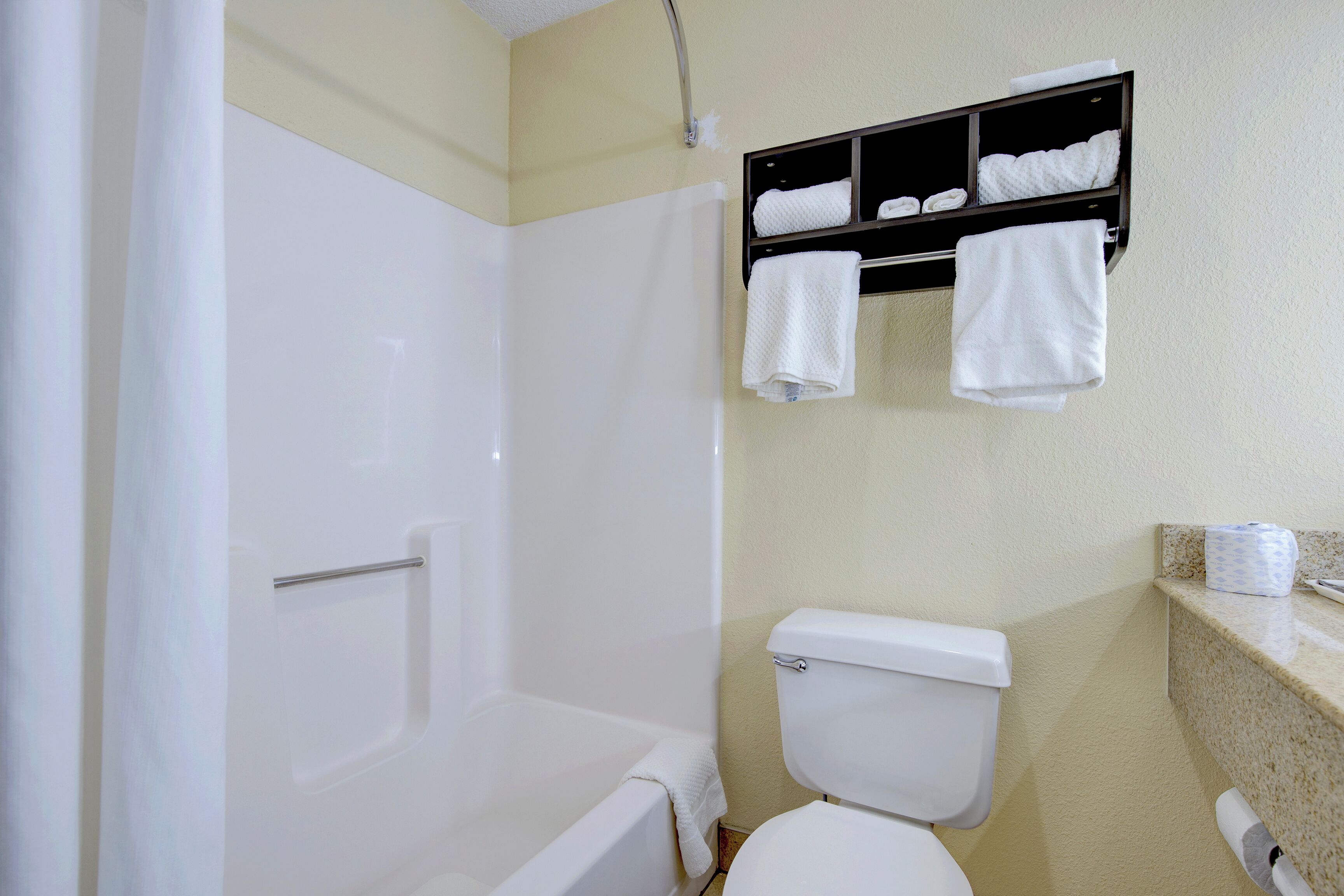 A bathroom with a bathtub, toilet, and a towel rack with multiple towels.