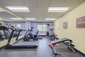 Un gimnasio con cintas de correr, elípticas y equipo de levantamiento de pesas.