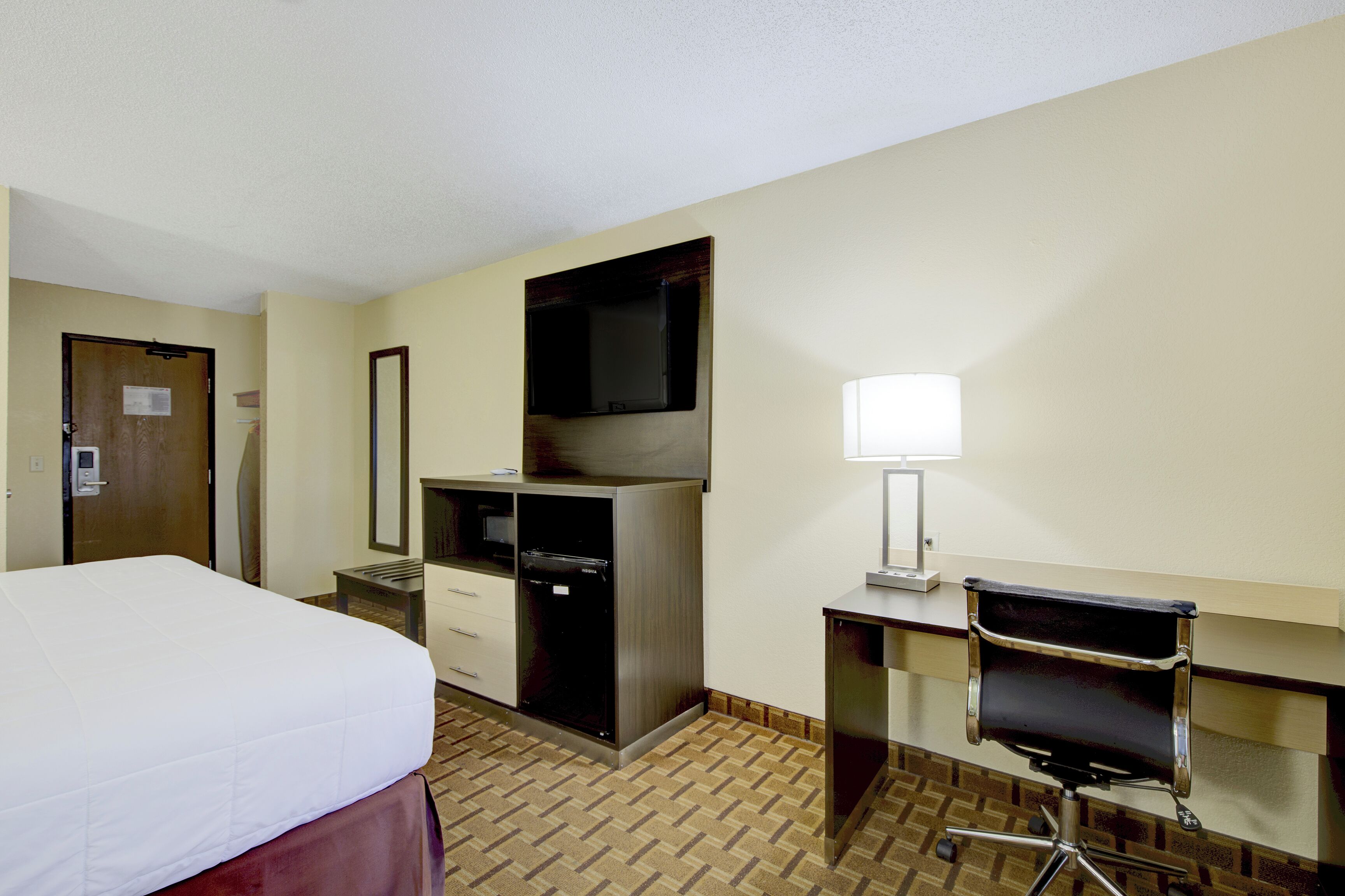 A hotel room with a bed, desk, chair, and a television.