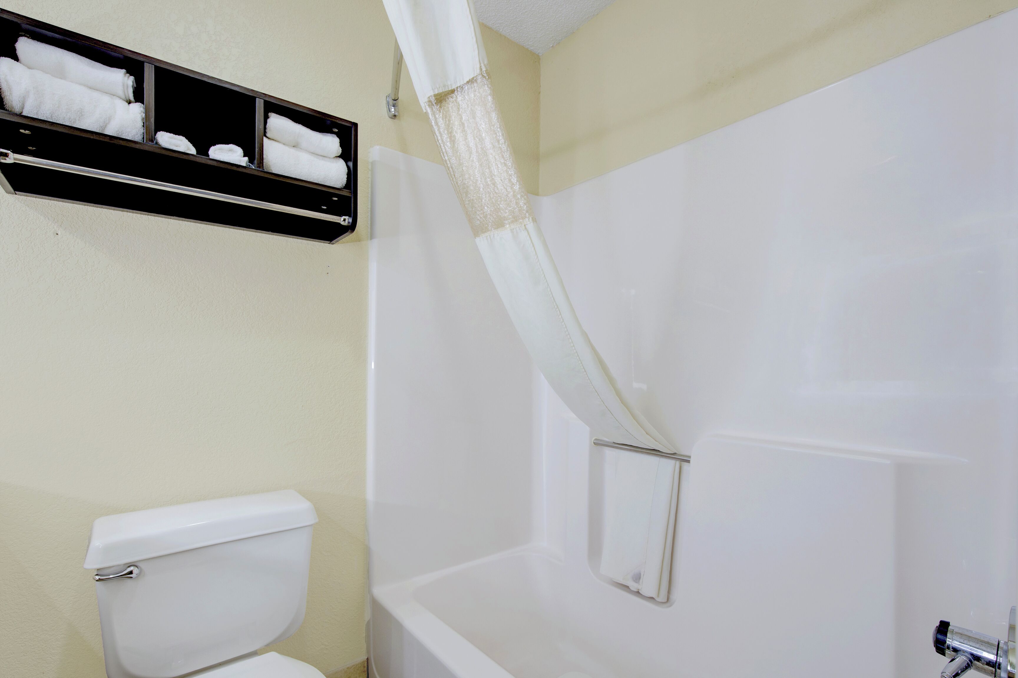 Un bagno con il water bianco, una vasca da bagno con tenda doccia e un portascopevoli con asciugamani piegati.