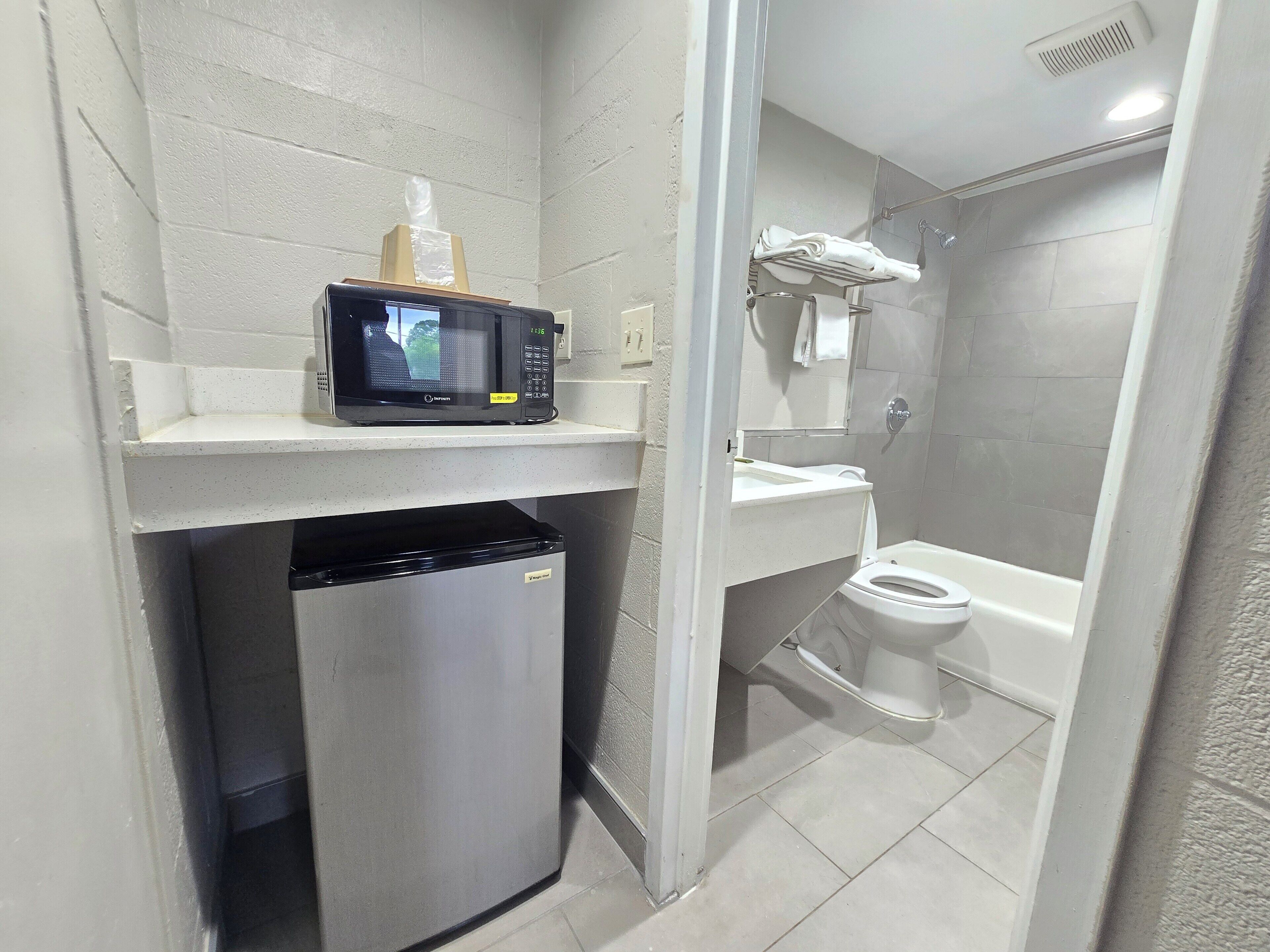 A compact bathroom with a microwave on a shelf, a toilet, and a shower area.