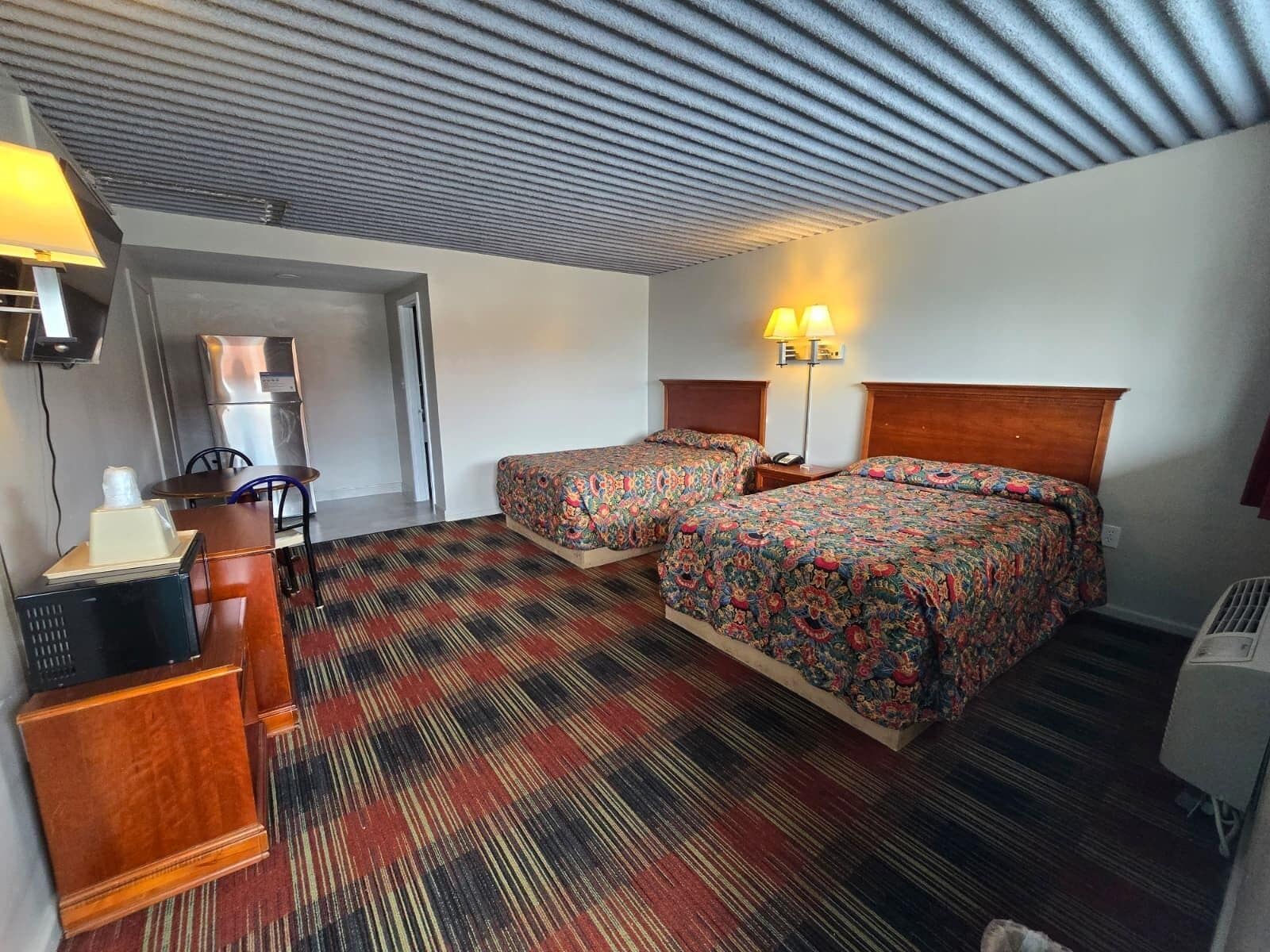 Habitación de hotel con dos camas, un escritorio, una silla, una lámpara y un refrigerador.