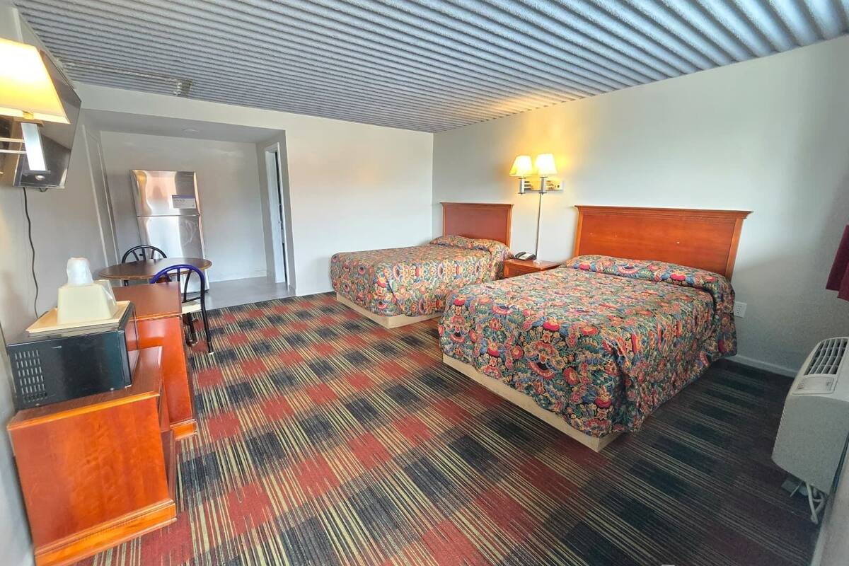 Habitació d'hotel amb dos llits, una taula, una cadira, un frigorífic i un sostre amb un relleu rugós.