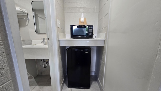 Un baño pequeño con lavamanos, microondas y un refrigerador compacto.