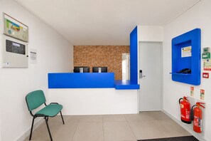 A reception area with a blue counter, a green chair, a brick wall, and fire extinguishers.