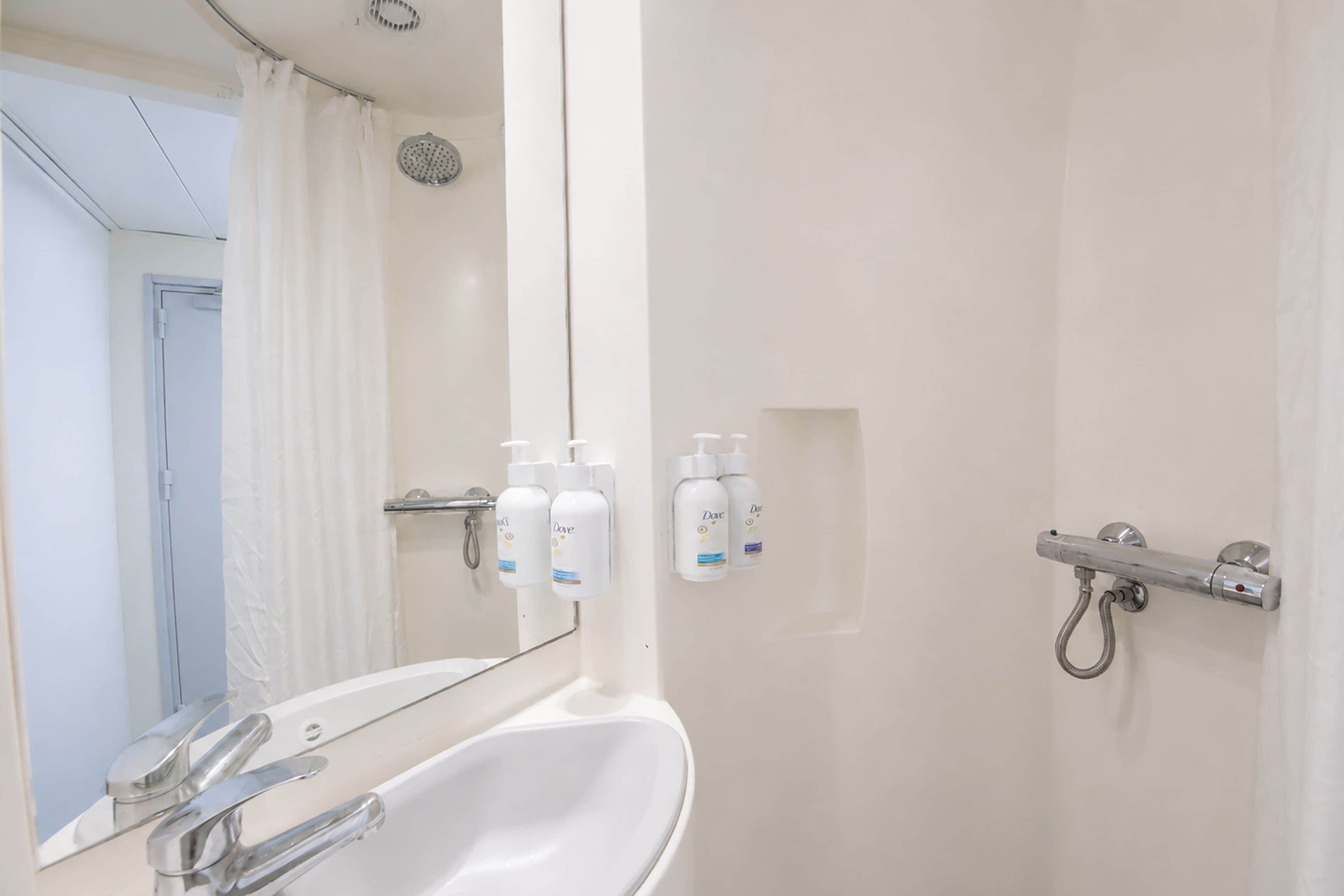 A bathroom with a sink, mirror, shower, and toiletries on the wall.