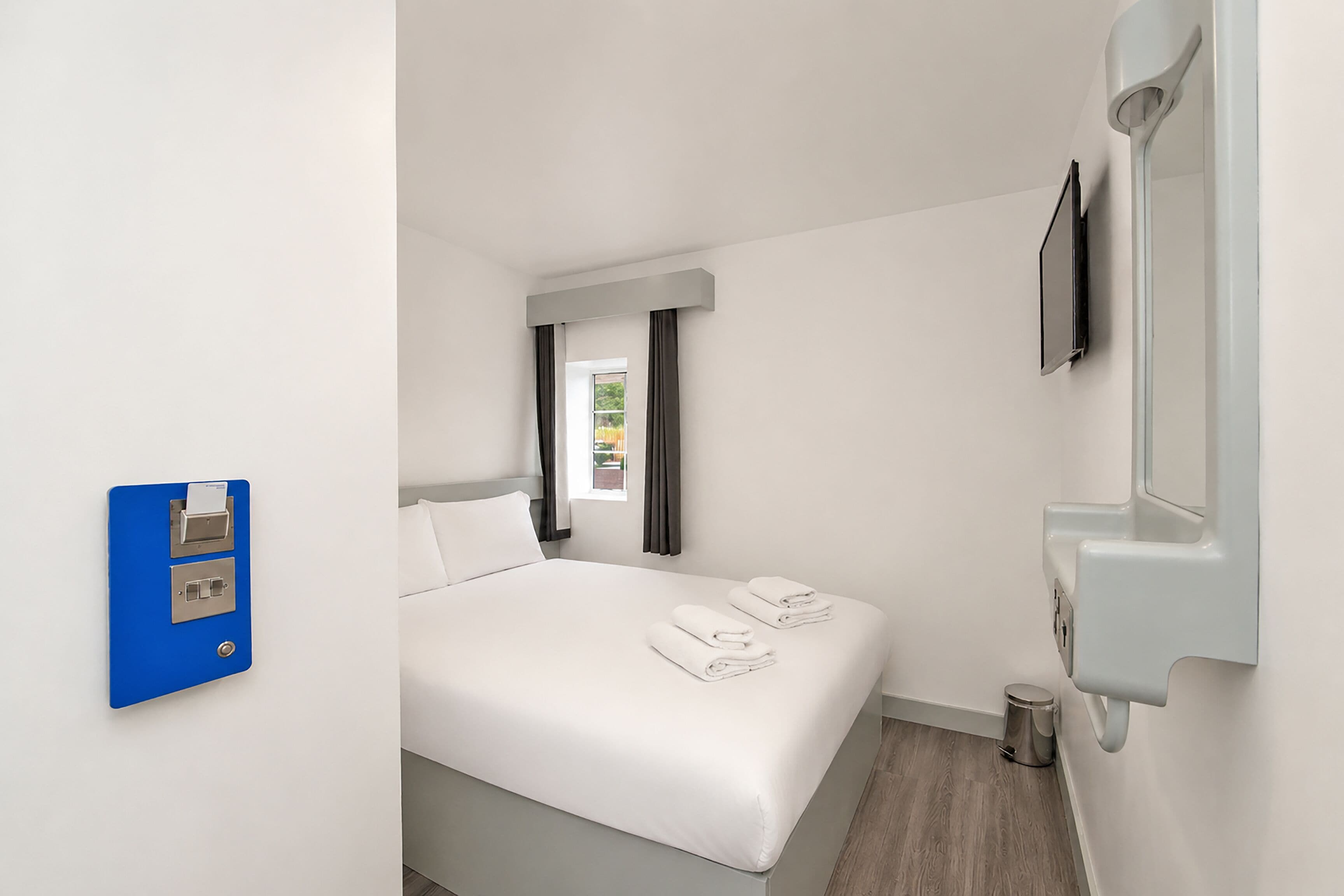 A hotel room with a bed, a TV, a sink, and a blue electrical panel.