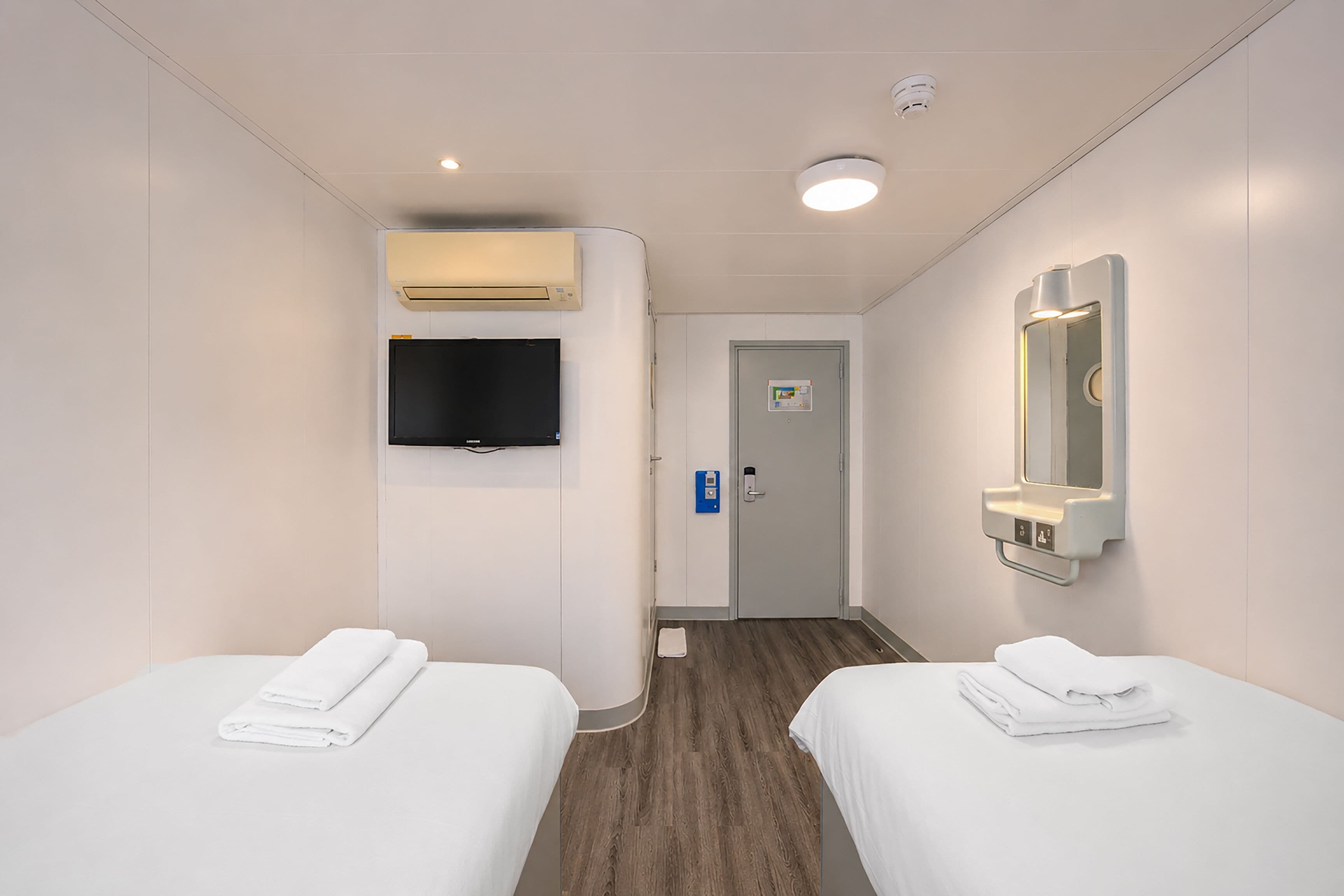 Ein Hotelzimmer mit zwei Betten, einem Flachbildfernseher, einem Spiegel und einer Tür mit einem Schild.