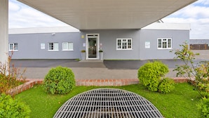 Ein Gebäude mit überdachter Eingangspartie, einem befestigten Einfahrtsweg und einem gepflegten Rasen mit Büschen.
