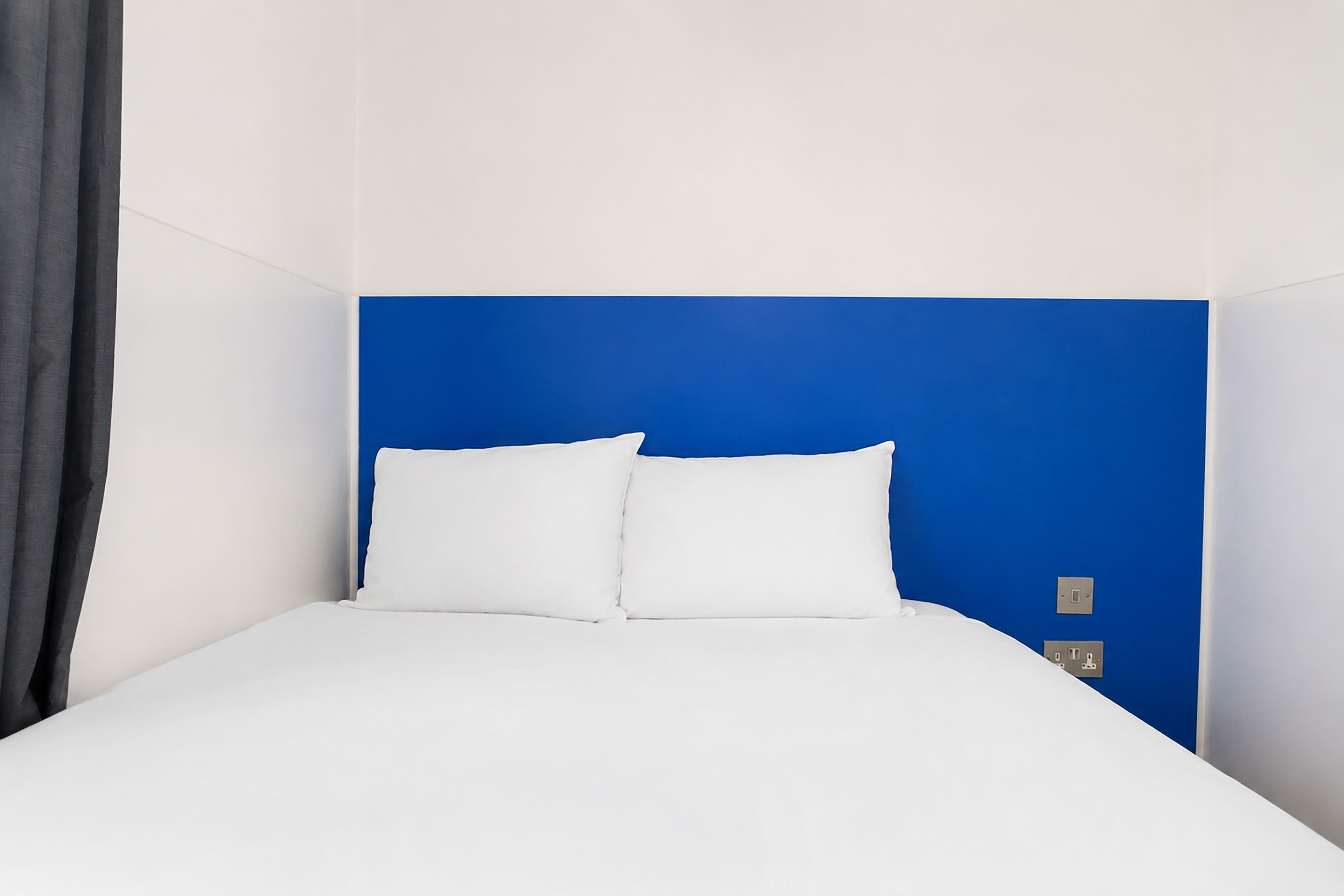 Ein Bett mit weißer Bettwäsche, einem blauen Kopfteil und zwei weißen Kissen.