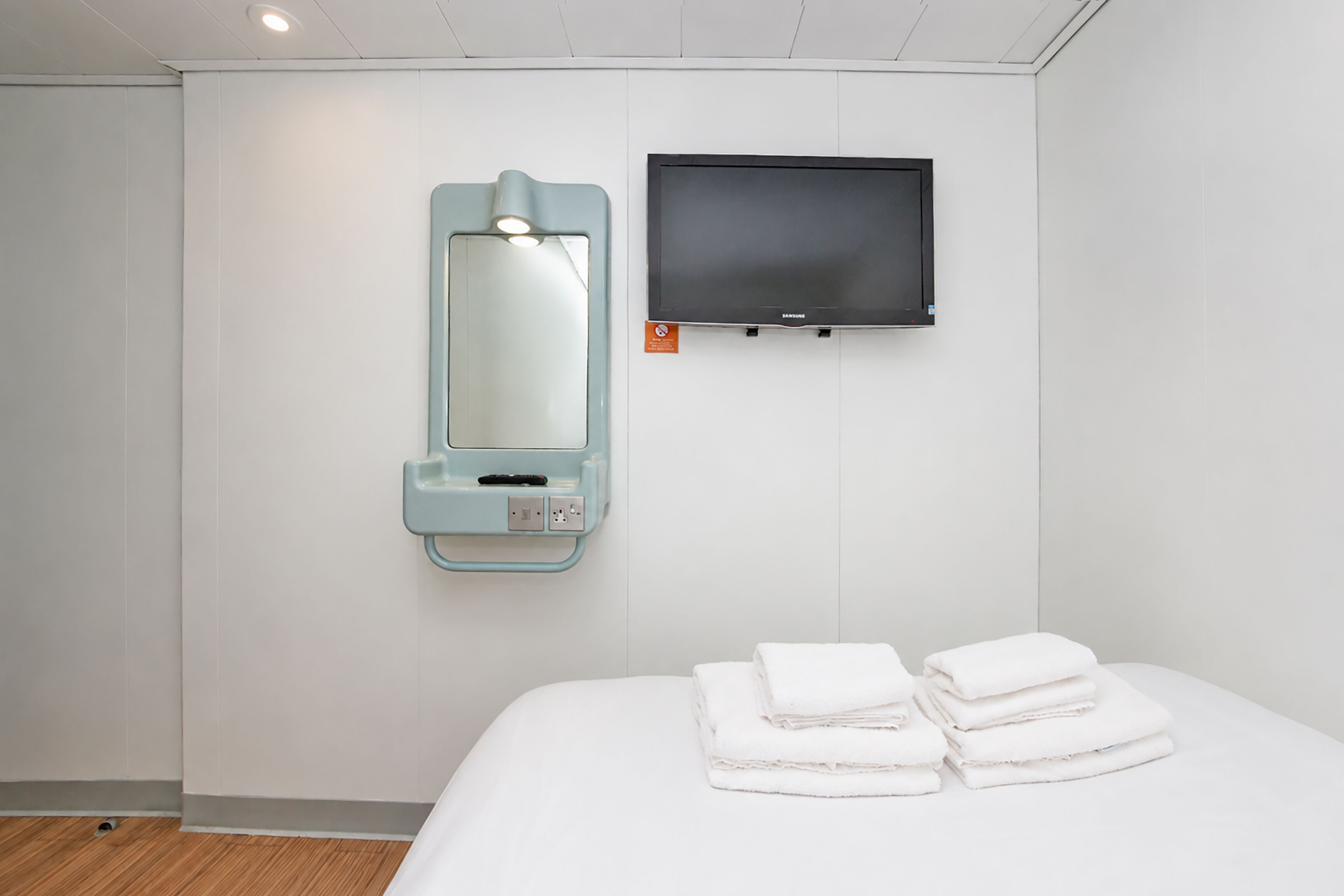 A hotel room with a bed, a wall-mounted TV, and a mirror with a light.