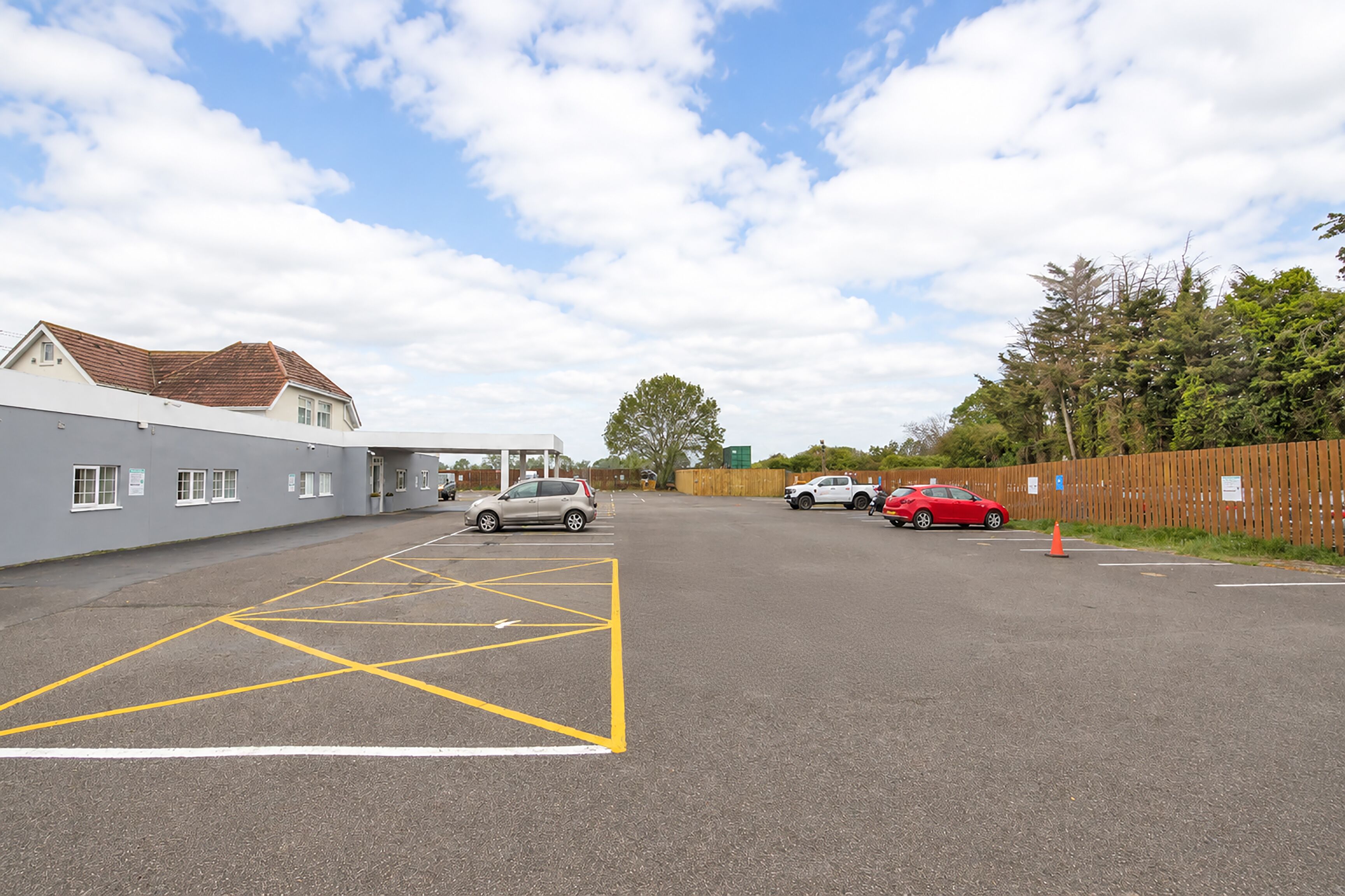 A parking lot with marked spaces, a building with a sloped roof, and a fence.