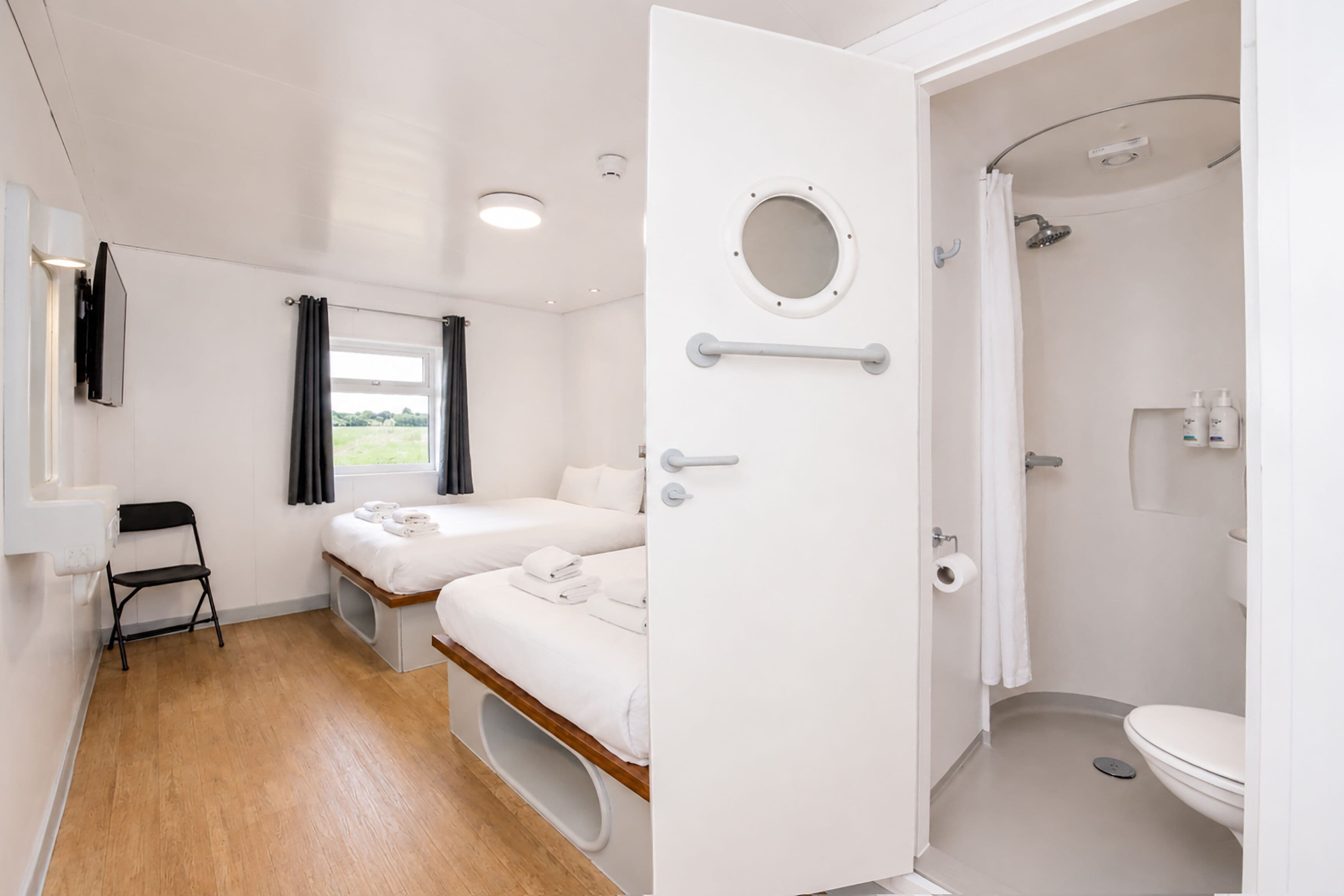 Een kamer met een bed, een tafeltje, een stoel, een raam met gordijnen, een deur naar een douche en een toilet.